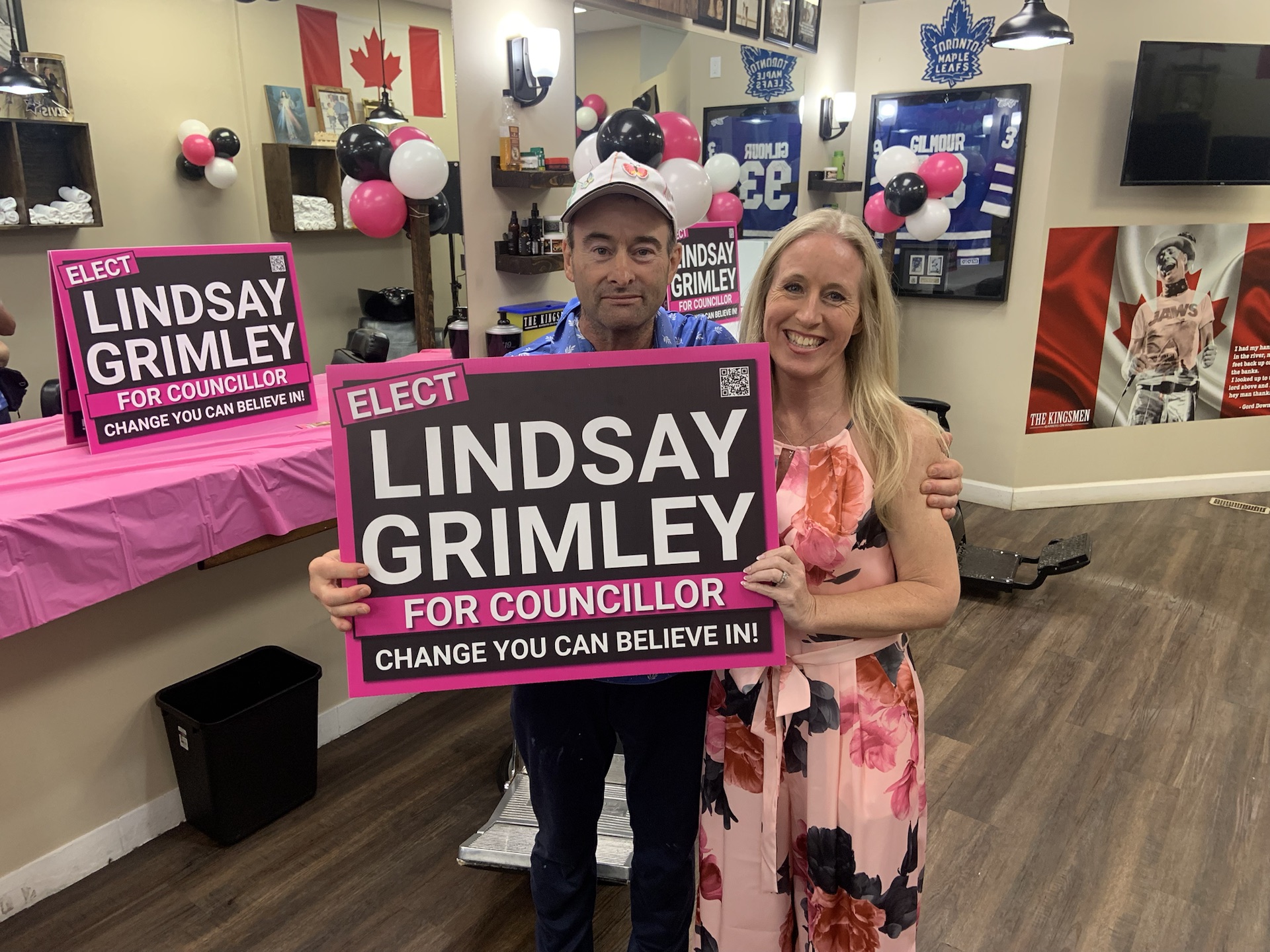 Lindsay Grimley with a supporter holding a campaign sign among pink, black, and white balloons at the launch party