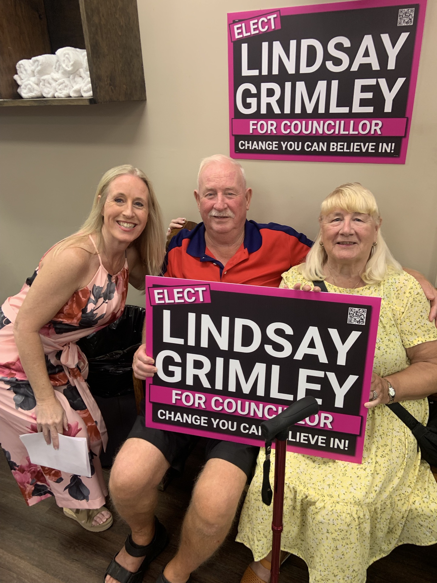 Lindsay Grimley with two seated guests holding a campaign sign at the launch party