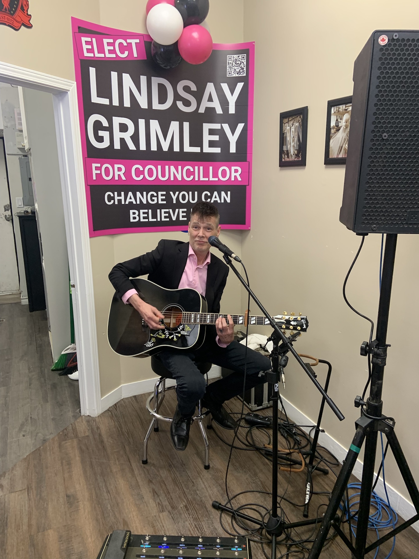 A musician playing guitar and singing at the campaign launch party in front of a Lindsay Grimley for Councillor poster